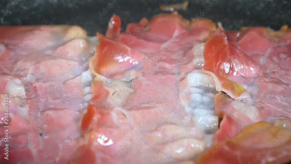 Thin pieces of smoked bacon being fried in a pan.