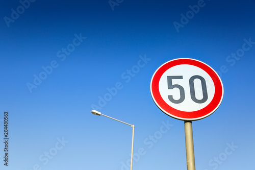 Traffic sign speed limit on the background of blue cloudless sky and street lamp.