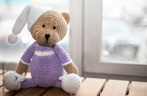 Brown stuffed animal teddy bear in lilac clothes and white hat. Copy space. Selective focus photo