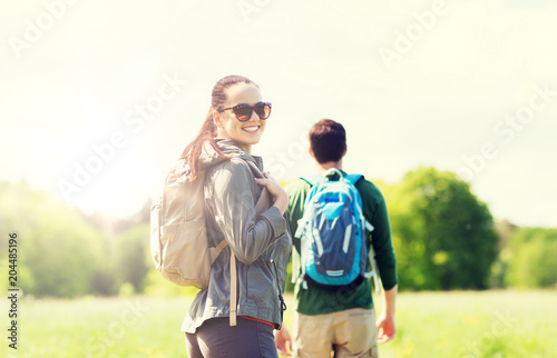 travel, hiking, backpacking, tourism and people concept - happy couple with backpacks walking along country road outdoors