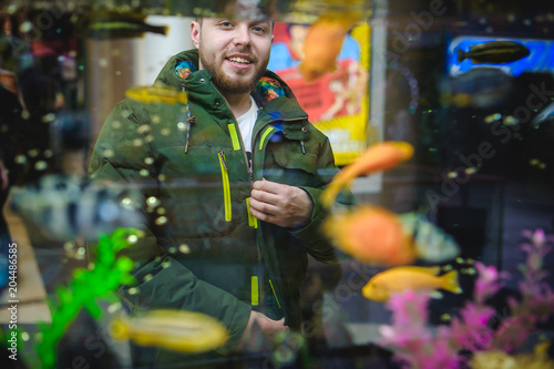 man looks at tropical fish in aquarium
