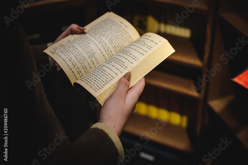 book in female hands on the background of a bookshelf