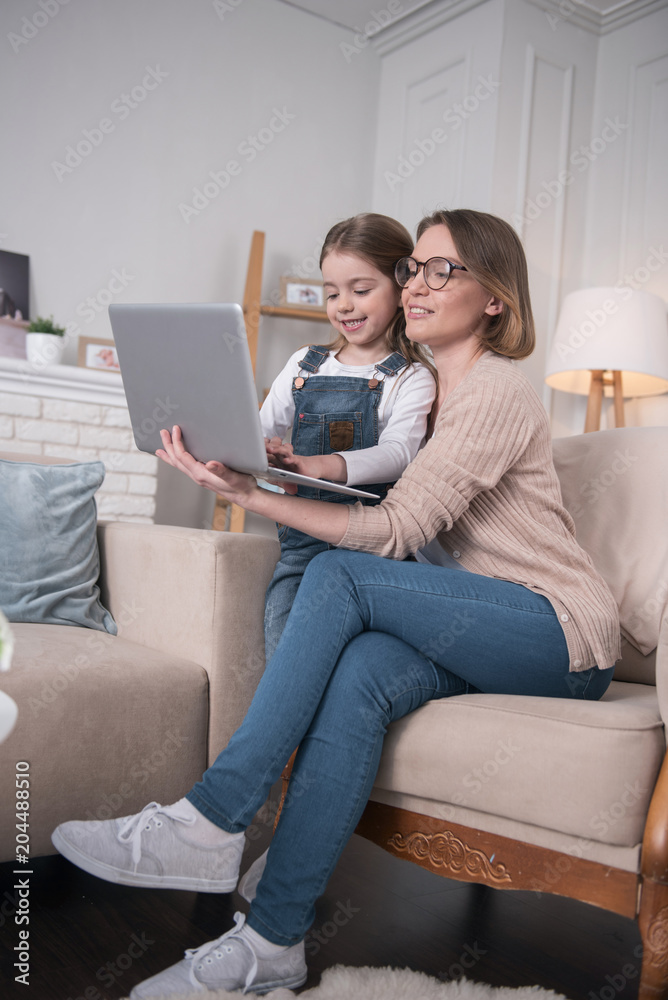Mastering laptop. Pretty exuberant mother sitting with her daughter and typing on the laptop Mastering laptop. Pretty exuberant mother sitting with her daughter and typing on the laptop