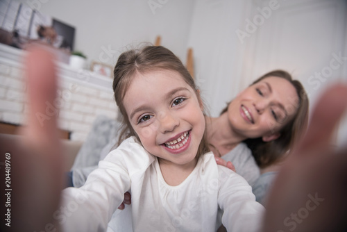 Time for fun. Beautiful cheerful mummy and daughter smiling and taking selfies