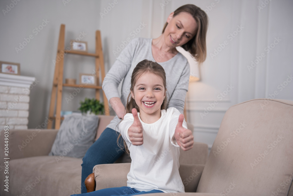 So happy. Exuberant nice girl sitting on the sofa and her mom combing her hair So happy. Exuberant nice girl sitting on the sofa and her mom combing her hair