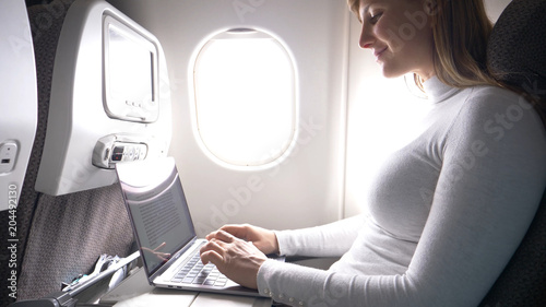 CLOSE UP: Happy businesswoman is typing on her high tech laptop during flight.