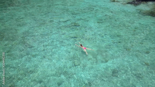 AERIAL  Flying above lonely Caucasian woman swimming in crystal clear ocean.