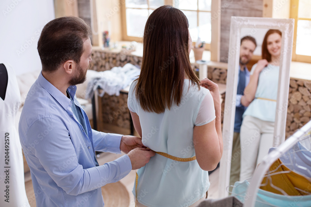 Obraz premium Needed alteration. Appealing craftsman taking measurements while standing with female customer