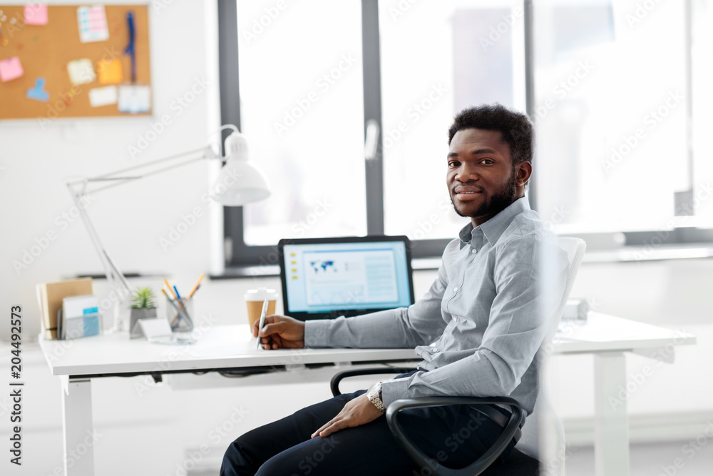 business and people concept - african american businessman with pen sitting at office table