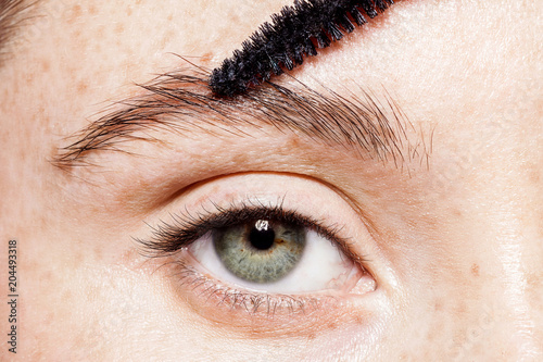 Close-up of female blue eye without make-up. Professional care for face concept. Master making corrects and gives shape previously painted brow with eyebrow brush