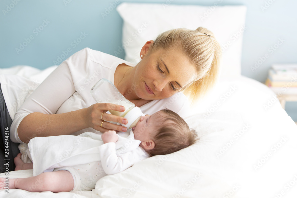 young, beautiful mother is feeding her cute baby daughter with a small bottle, filled with milk