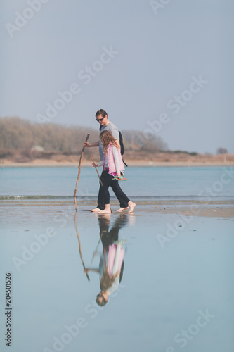 Water reflection of middle aged man and daughter walking on the beach