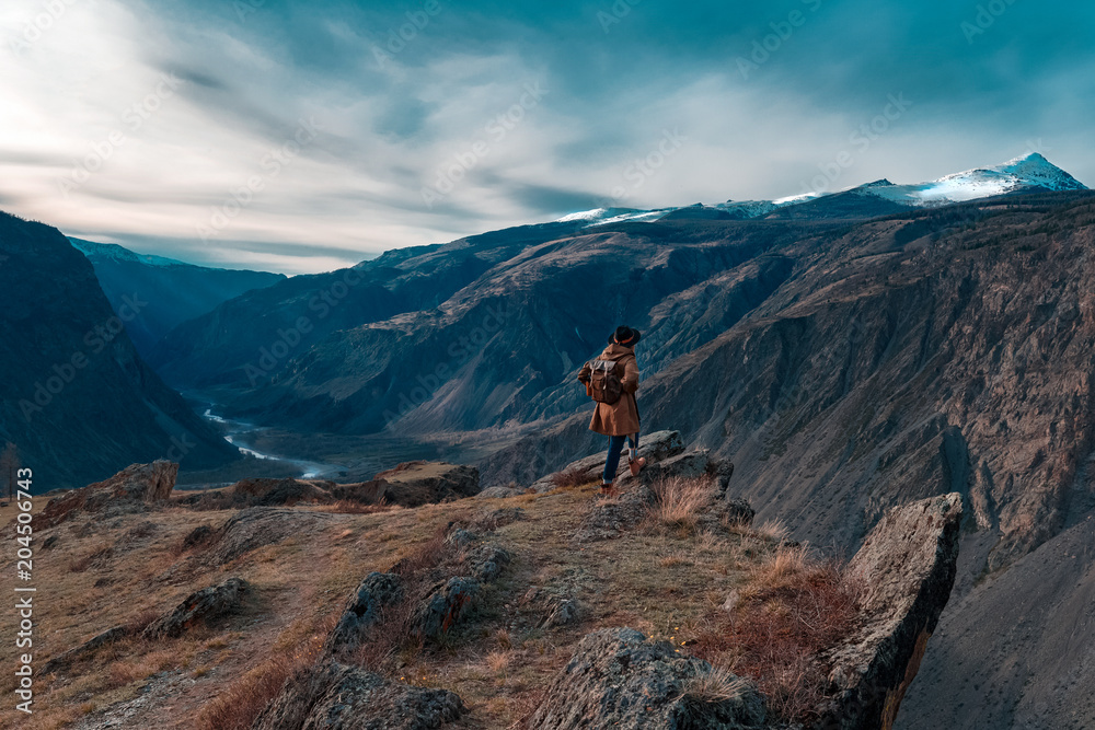 Beautiful young woman with retro backpack on the top of cliff amazing mountain range landscape. Sunset. Hipster. Adventure. Travel lifestyle. Copy space.