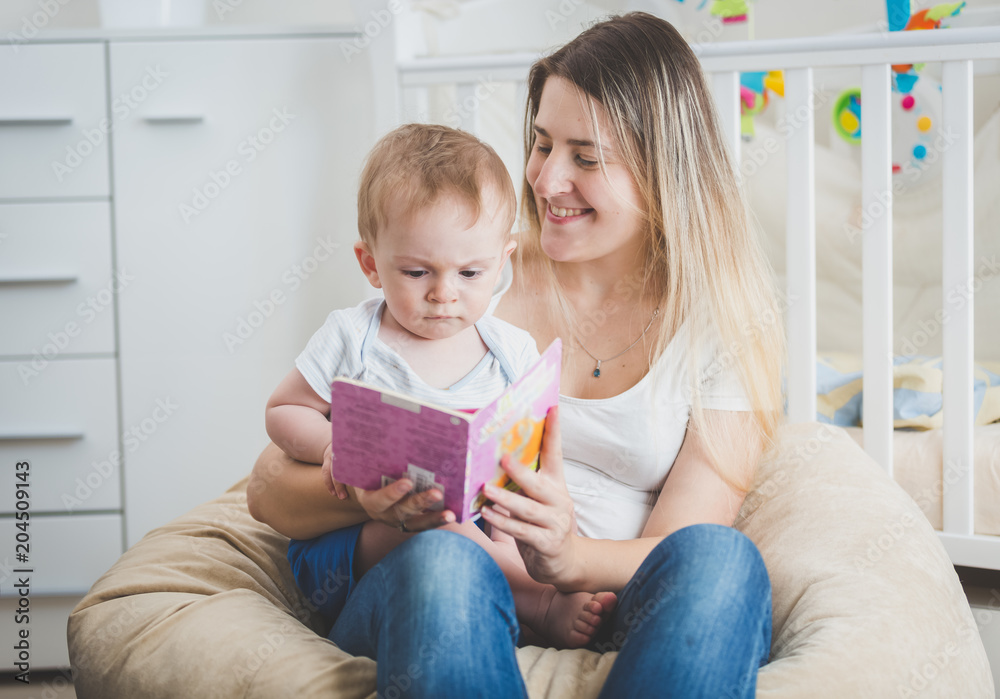 Beautiful smiling young mother reading fairy tale to her baby boy sitting on her lap Beautiful smiling young mother reading fairy tale to her baby boy sitting on her lap