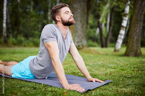 Young man doing yoga outdoors in the morning during summer