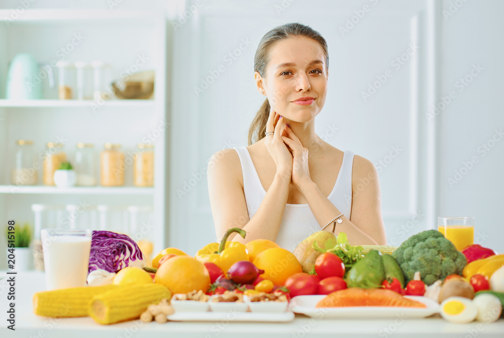 happy young housewife sitting in the kitchen preparing food from a pile of diverse fresh organic fruits and vegetables, selective focus happy young housewife sitting in the kitchen preparing food from a pile of diverse fresh organic fruits and vegetables, selective focus