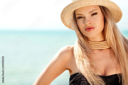 Beautiful fit woman in black swim suit and hat posing on the beach. Summer vacation.