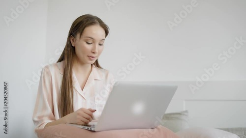 young and cute woman talking to friends on social networks holding laptop on her feet in the bedroom photo