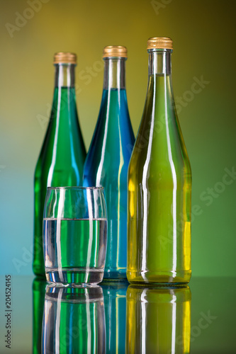 a glass of water and bottles on a colorful background