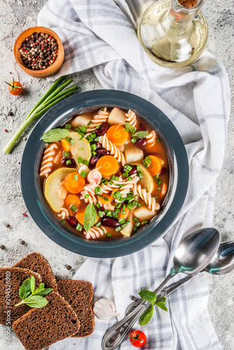 Italian vegetable soup Minestrone with fusilli pasta,  vegetarian food concept, grey stone background, copy space