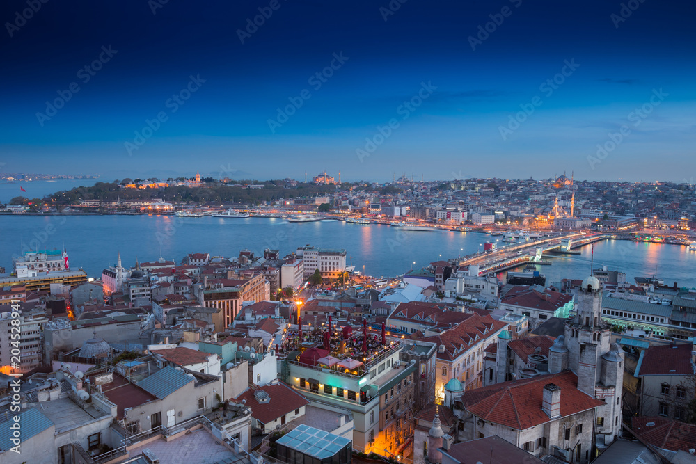 Long exposure panoramic cityscape of Istanbul at a warm calm evening from Galata to Golden Horn gulf. Wonderful romantic old town at Sea of Marmara. Bright light of street lighting. Istanbul. Turkey.