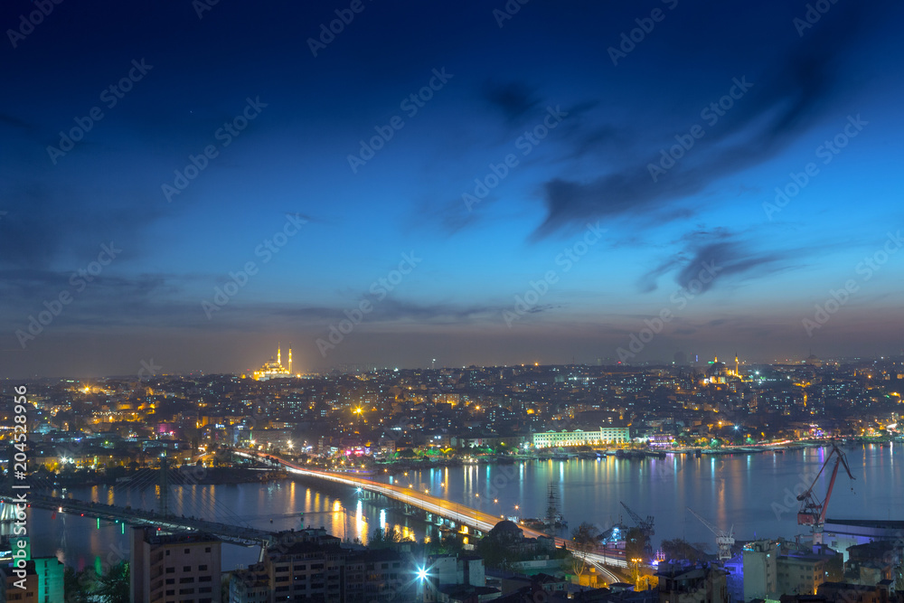 Fototapeta premium Long exposure panoramic cityscape of Istanbul at a warm calm evening from Galata to Golden Horn gulf. Wonderful romantic old town at Sea of Marmara. Bright light of street lighting. Istanbul. Turkey.