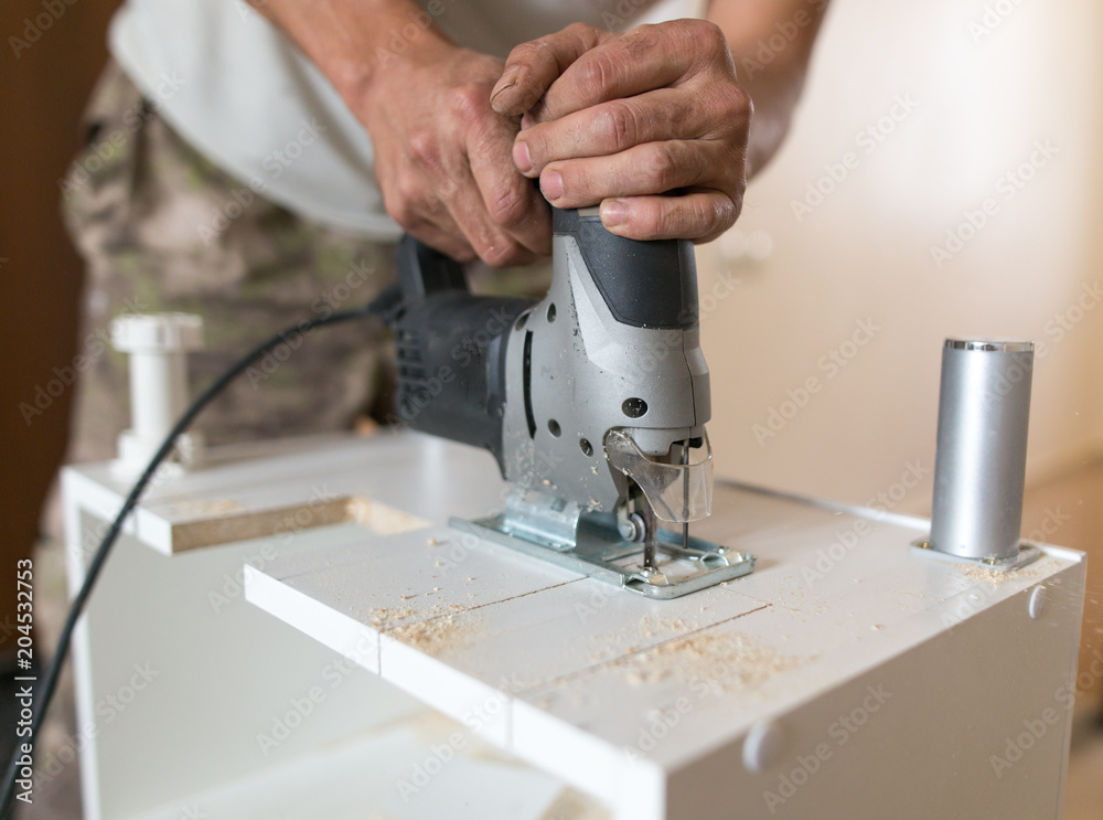 A man cuts out a wooden board with a jigsaw A man cuts out a wooden board with a jigsaw