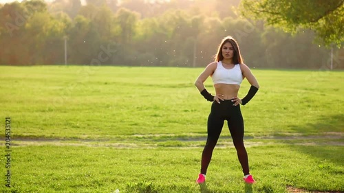 Young beautiful woman listening music at park while running. Portrait of smiling sporty girl with earphone looking at camera at park in autumn. Woman athlete looking at camera during winter sunset. photo
