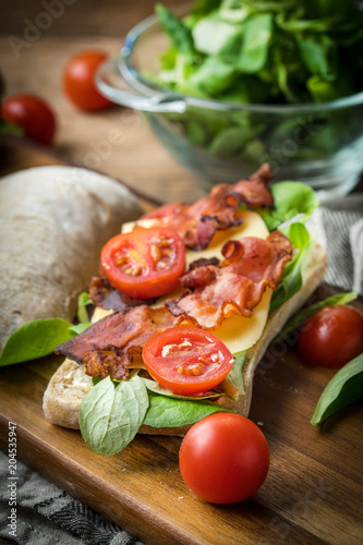 Ciabatta sandwich with arugula salad, bacon and yellow cheese.