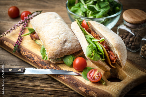 Ciabatta sandwich with arugula salad, bacon and yellow cheese.