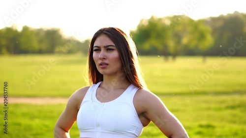 Young beautiful woman listening music at park while running. Portrait of smiling sporty girl with earphone looking at camera at park in autumn. Woman athlete looking at camera during winter sunset. photo