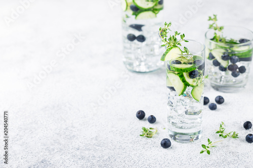 Detox infused flavored water with blueberry, cucumber and thyme on white background. Refreshing summer homemade cocktail