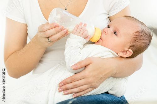 Closeup photo of young woman holding her baby on lap and giving him bottle of milk