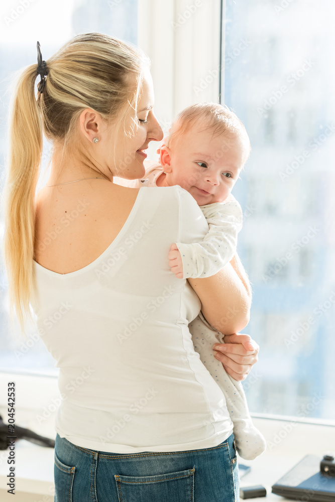 Beautiful young woman holding her 3 months old baby at big window Beautiful young woman holding her 3 months old baby at big window