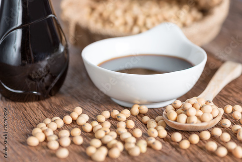 Soy sauce in bowl with bottle and soy bean on wood table.