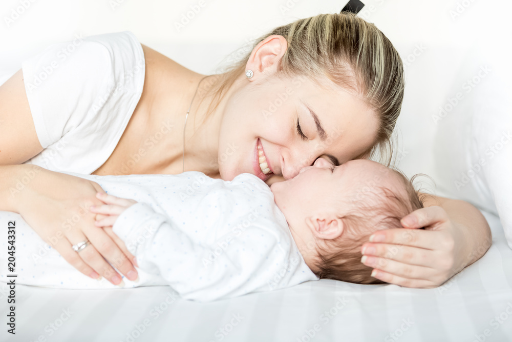 Portriat of happy young mother with closed eyes lying on bed next to her 3 months old baby boy