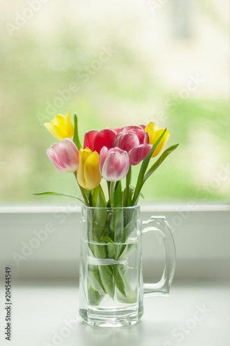piccoli tulipani colorati su una finestra bianca in una tazza di vetro