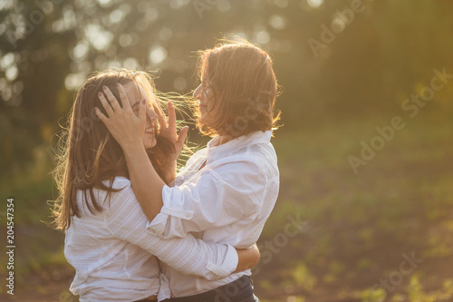 a woman with a daughter as a teenager huggingon the nature in the soft sunset light