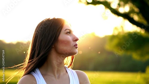 Young beautiful woman listening music at park while running. Portrait of smiling sporty girl with earphone looking at camera at park in autumn. Woman athlete looking at camera during winter sunset. photo
