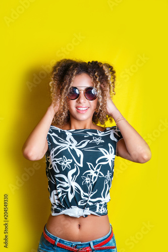 Beauty portrait of young african american girl with afro hairstyle. Girl posing on yellow background, looking at camera. Studio shot.