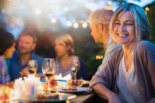 Group of friends gathered around a table in a garden on a summer evening to share a meal and have a good time together. Focus on a beautiful woman