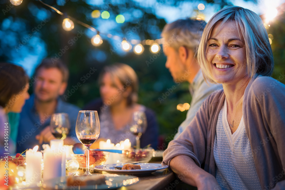 Group of friends gathered around a table in a garden on a summer evening to share a meal and have a good time together. Focus on a beautiful woman Group of friends gathered around a table in a garden on a summer evening to share a meal and have a good time together. Focus on a beautiful woman
