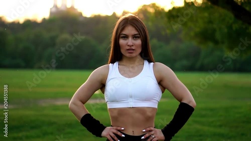 Young beautiful woman listening music at park while running. Portrait of smiling sporty girl with earphone looking at camera at park in autumn. Woman athlete looking at camera during winter sunset. photo