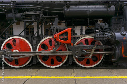 fragment of vintage functioning steam locomotive standing at station, closeup, visible driving wheels with a system of pistons, connecting rods and levers