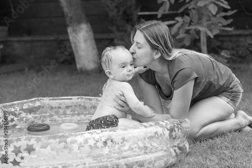 Black and white photo of happy young mother kissing her baby swimming in inflatable swimming pool
