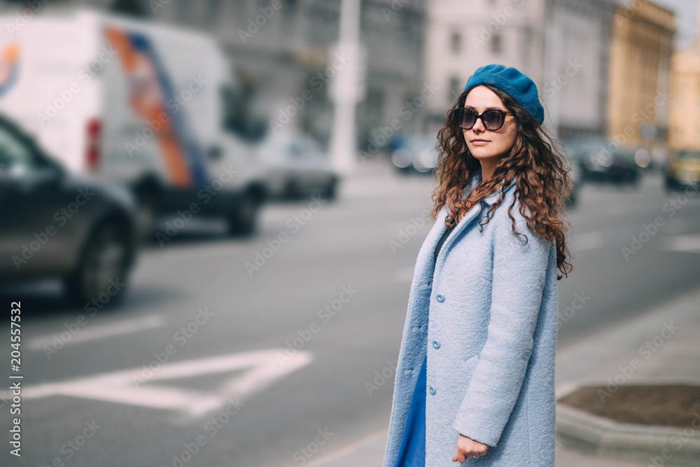 long-haired young woman in a blue beret and sunglasses walking around the city.