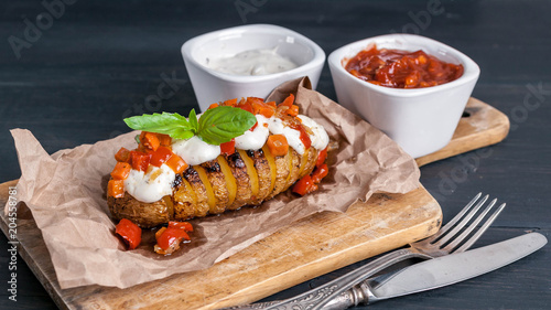 Baked potatoes with mozzarella cheese, vegetables and spices. Cheese and tomato sauces. Fork and knife