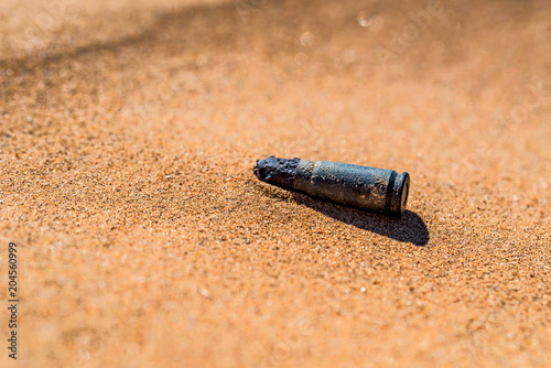 Old rusty cartridge case in sand close photo