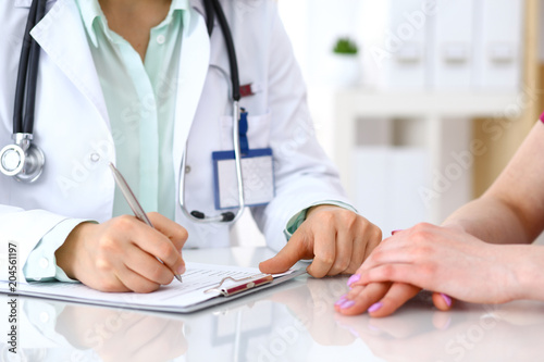 Female doctor filling up an application form while consulting patient. Just hands. Medicine and health care concept