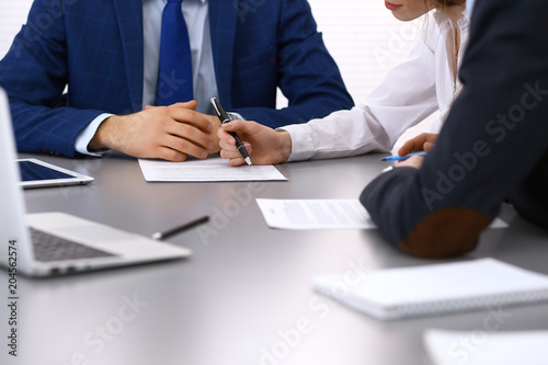 Group of business people and lawyer discussing contract papers sitting at the table, closeup. Businessman is signing document after agreement done